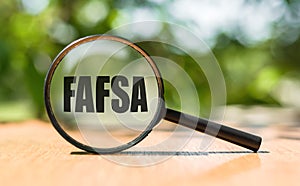 Free Application for Federal Student Aid - FAFSA written on magnifying glass on wooden table and green background. Concept image