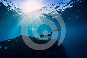 Free diver girl in pink swimwear with fins swimming underwater at wreck ship. Freediving in the ocean