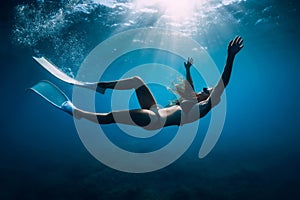 Free diver woman with white fins glides underwater with amazing sun rays. Freediving underwater in sea