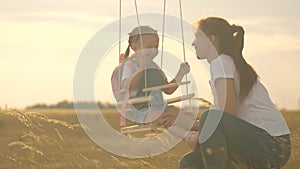 The free family is having fun in the park. mother shakes her healthy little daughter on a swing under a tree in the sun