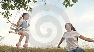 The free family is having fun in the park. mother shakes her healthy little daughter on a swing under a tree in the sun