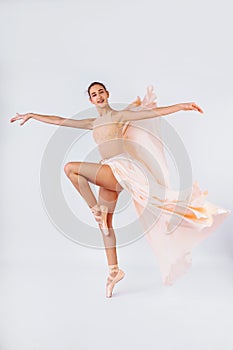 Free flight. Graceful classic ballerina dancing on white studio background. Pastel beige dress cloth. The grace, artist, movement