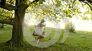 Free girl swinging on a swing on an oak branch in sun. Dreams of flying. Happy childhood concept. Beautiful girl in a