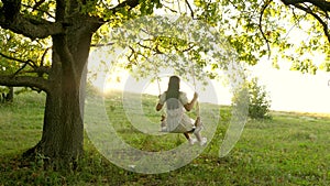 Free girl swinging on a swing on an oak branch in sun. Dreams of flying. Happy childhood concept. Beautiful girl in a