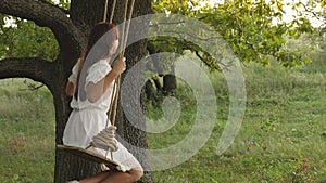 Free girl swinging on a swing on an oak branch in sun. Dreams of flying. Happy childhood concept. Beautiful girl in a