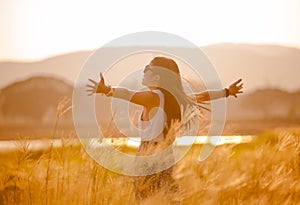 Free happy woman enjoying sunset. Beautiful woman in white dress embracing the golden sunshine glow of sunset with arms outspread