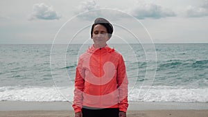 Free happy young woman is looking at camera with seascape on background, enjoying stormy windy day in nature, breathing fresh air,