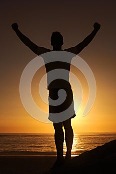 Free at last. Silhouette of a man standing with his arms victoriously raised against the sunset.