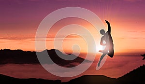 Free Man Jumps For Joy On The Top of Mountain Peak Above Clouds At Sunset. Young Successful Happy Person Jumping