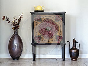 A free standing antique wood cabinet, flower vase, and metal pitcher