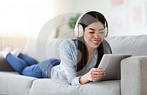 Free Time. Smiling Korean Girl Using Digitral Tablet And Headphones At Home