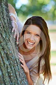 Free to be myself. Portrait of a beautiful young woman standing behind a tree at the park.