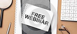 FREE WEBINAR on notepad and various business papers on brown background. Brown glasses and magnifier with notepad
