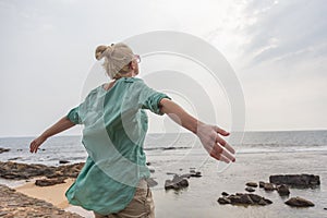 Free woman enjoying windy weather on beach on overcast day