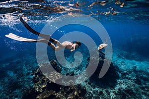 Freediver with fins glides underwater with turtle in ocean. Snorkeling with sea turtle