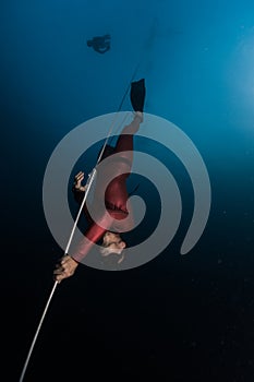 Freediver in red wetsuit descends along the rope