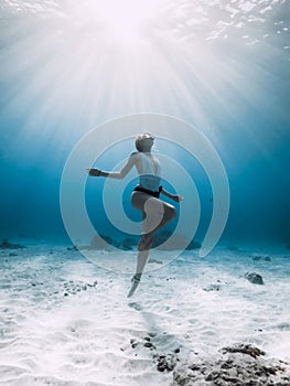 Freediver underwater. Freediving with woman in blue ocean with sandy bottom and sun rays