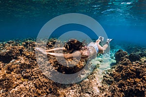 Freediver woman glides with fins over coral reef in tropical sea