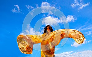 Una bella Caucasica donna danzante con golden movimento scialle ali davanti al cielo azzurro di sfondo.