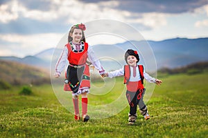 Freedom bulgarian girl and boy with traditional ethnic folklore costumes running on a green lawn in the countryside in Bulgaria