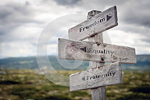 Freedom, equality and fraternity text on wooden sign post outdoors in landscape scenery.