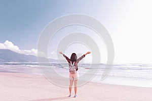 Freedom feel good and travel adventure concept. Happy backpacker woman raise hand up at tropical sunset beach abstract background