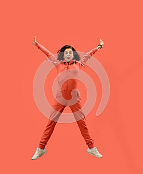 Freedom in moving. Pretty young woman jumping against coral background