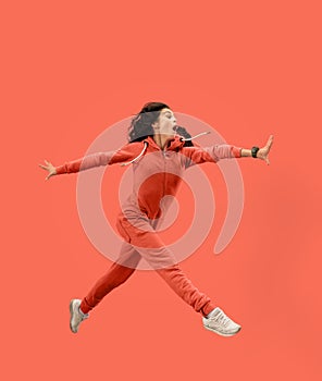 Freedom in moving. Pretty young woman jumping against coral background