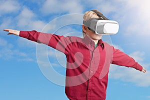 Freedom, technology and entertaiment concept. Small male child in red shirt wears VR glasses, studies possibilities of gadget, ima