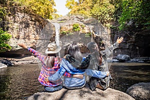 Freedom traveler group of woman sitting waterfall front on stone and raised arms enjoying a beautiful nature.