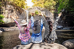 Freedom traveler group of woman sitting waterfall front on stone and raised arms enjoying a beautiful nature.