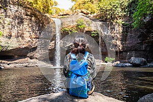 Freedom traveler woman alone sitting waterfall front on stone with bag and a beautiful nature.