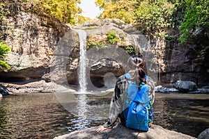 Freedom traveler woman alone sitting waterfall front on stone with bag and a beautiful nature.