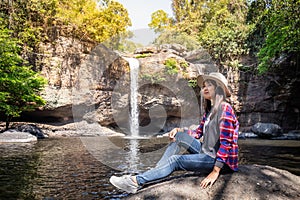 Freedom traveler woman alone sitting waterfall front on stone with bag and hat and a beautiful nature.