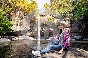 Freedom traveler woman alone sitting waterfall front on stone with bag and hat and a beautiful nature.