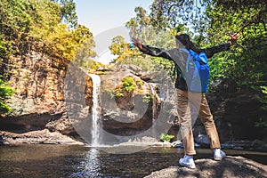 Freedom traveler woman standing waterfall front on stone with bag and raised arms enjoying a beautiful nature.