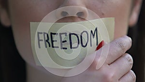 Freedom written on tape, woman removing mouth sticker, rights oppression, block