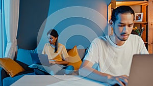 Freelance asia couple man and woman in casual feel serious focus on work separate laptop computer at night, hasband sit in front