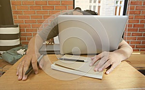 Freelance Asian man worker sleeping on laptop with notebook and