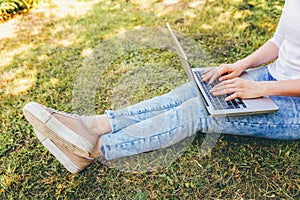 Freelance business concept. Woman legs on green grass lawn in city park, hands working on laptop pc computer. Lifestyle authentic