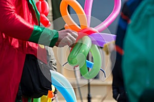 A freelance clown creating balloon animals and different shapes at outdoor festival in city center.