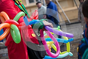 A freelance clown creating balloon animals and different shapes at outdoor festival in city center.