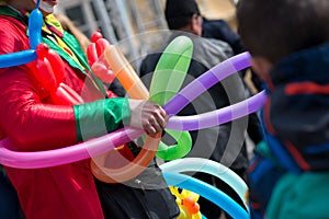 A freelance clown creating balloon animals and different shapes at outdoor festival in city center.