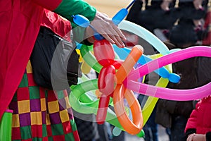 A freelance clown creating balloon animals and different shapes at outdoor festival in city center.