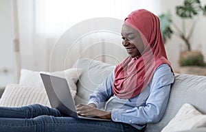 Freelance Concept. Joyful black islamic woman working remotely on laptop at home