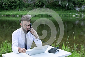 freelance concept, work outside office, remote work. bearded man works behind laptop in the open air. calls by phone