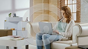 Freelance girl typing on laptop sitting on sofa, comfortable working conditions