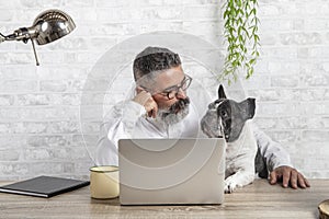 Freelance man working from home with his dog sitting in the office. Man using a laptop at home with a cute dog