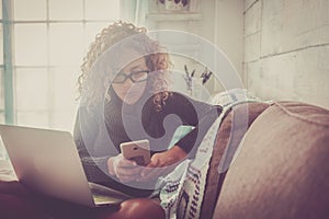 Freelance people at work at home - beautiful adult caucasian woman sit on the sofa with phone device and laptop computer working -