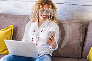 Freelance people at work at home - beautiful adult caucasian woman sit on the sofa with phone device and laptop computer working -